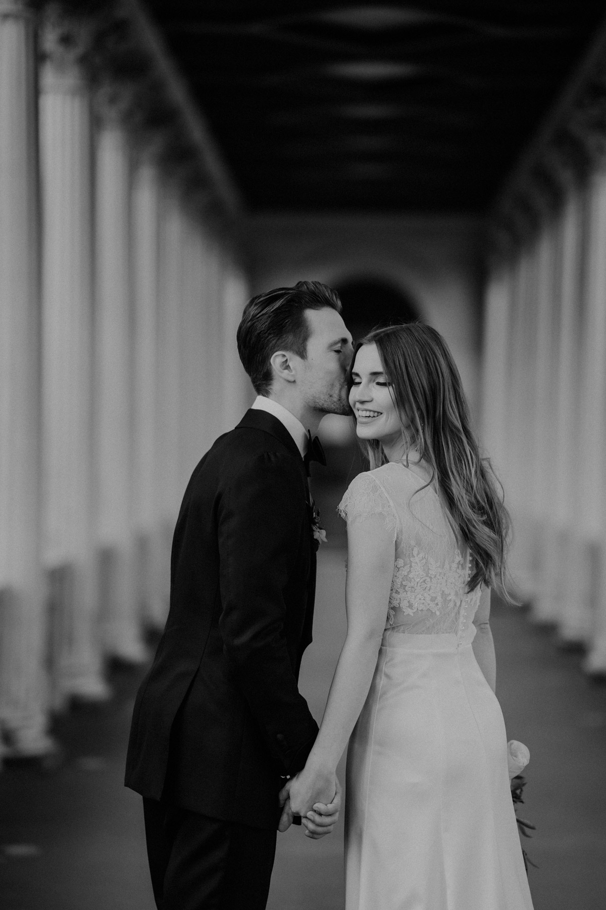 Rückenansicht des Paares: Bräutigam küsst Braut sanft auf die Schläfe