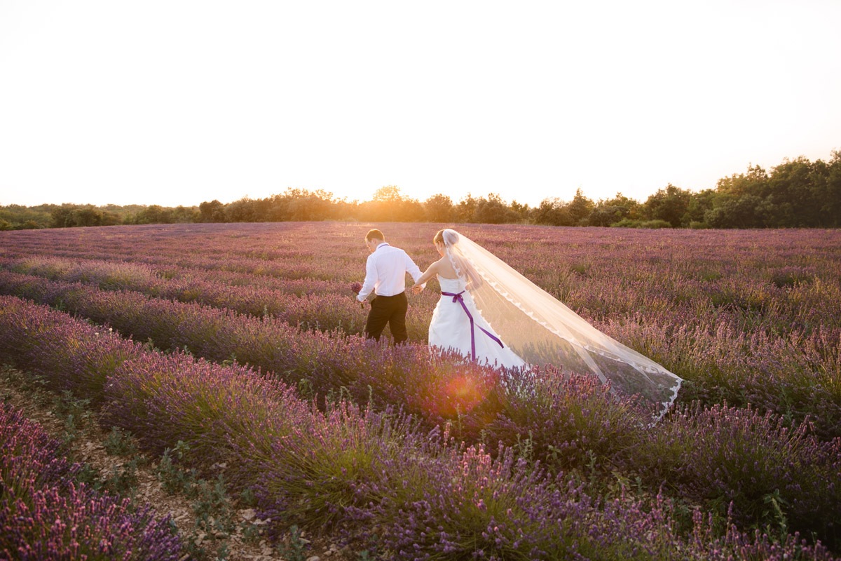 After-Wedding-Shooting in der Provence: Brautpaar im Lavendelfeld bei Sonnenuntergang. Die lila Schleife am Brautkleid harmoniert mit dem Lavendel. Ein Beispiel für entspannte Hochzeitsfotos nach der Hochzeit von Hochzeitsfotografin Berlin.