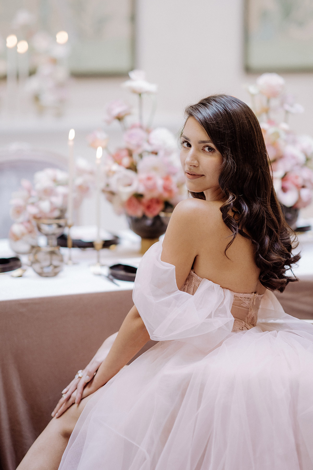 Elegantes Brautporträt im Hotel Adlon Berlin: Die Nutzung lichtstarker Festbrennweiten erzeugt ein cremiges Bokeh und eine starke Freistellung der Braut im rosa Kleid vor der Hochzeitstafel.