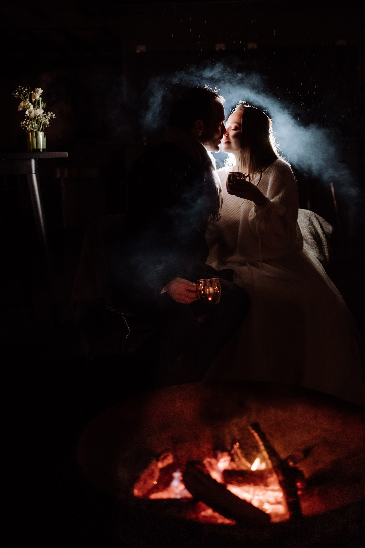 Romantischer Moment am Lagerfeuer im heimlichTreu Berlin: Das Brautpaar sitzt im Winter bei Regen nachts im warmen Schein der Flammen. Ein Beweis für höchste fotografische Qualität und Lichtbeherrschung bei schwierigen Lichtverhältnissen von Hochzeitsfotografin Berlin.