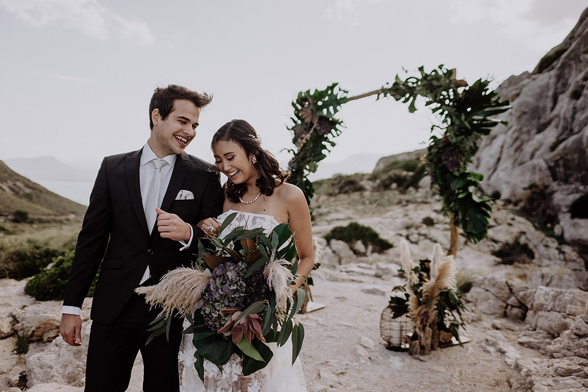 Strahlendes Brautpaar im Boho-Stil beim Auszug nach der freien Trauung unter freiem Himmel. Emotionaler Moment einer Hochzeitsbegleitung in Foto und Video auf Mallorca.