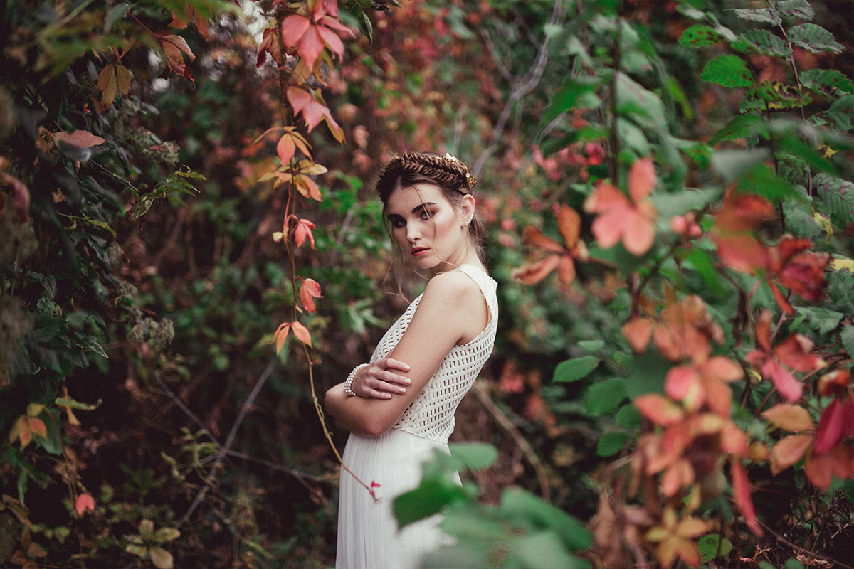 Porträt einer Braut in ausdrucksstarker Fashion-Pose, umgeben von herbstlichem Laub in Rot und Grün. Natürliche Hochzeitsfotografie in Berlin, die Ästhetik und Nachhaltigkeit durch digitale Bereitstellung und Alben auf Wunsch vereint.