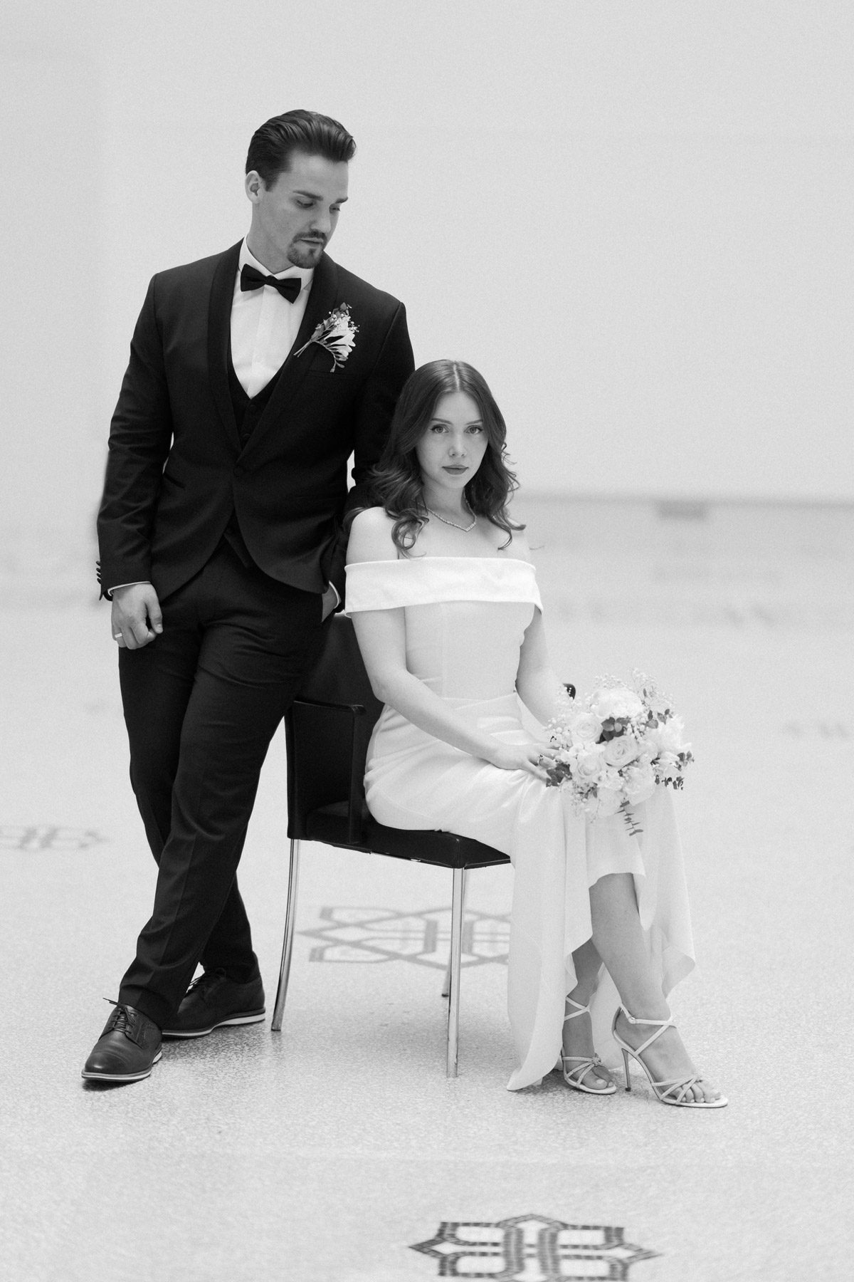 High-End Elopement-Fotografie im Hotel de Rome: Das Paar posiert im Editorial-Stil wie auf einem Magazin-Cover. Sie sitzt auf einem Stuhl, er steht daneben. Fokus auf zeitlose Eleganz und Fashion-Ästhetik.